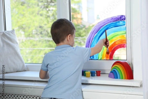 Fototapeta Little boy drawing rainbow on window indoors