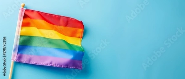 Fototapeta  Rainbow flag with wooden stick emerging from its side against a blue backdrop Include ample room for text or other elements