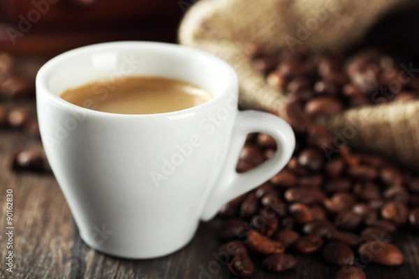 Fototapeta Cup of coffee with beans on table close up