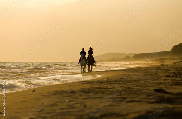 Fototapeta Horse rider couple at sunset beach, next to the sea