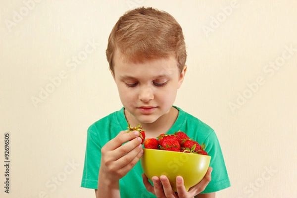 Fototapeta Little boy takes a fresh strawberry from the bowl