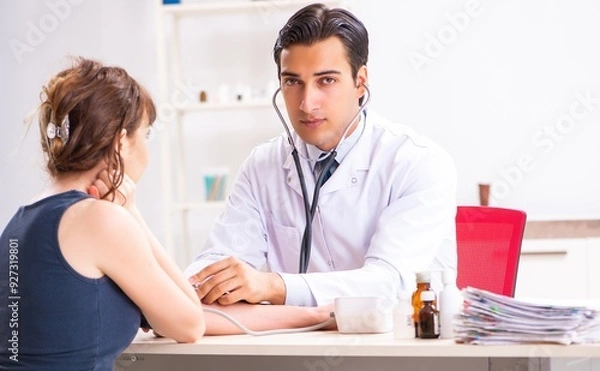 Fototapeta Young doctor checking woman's blood pressure