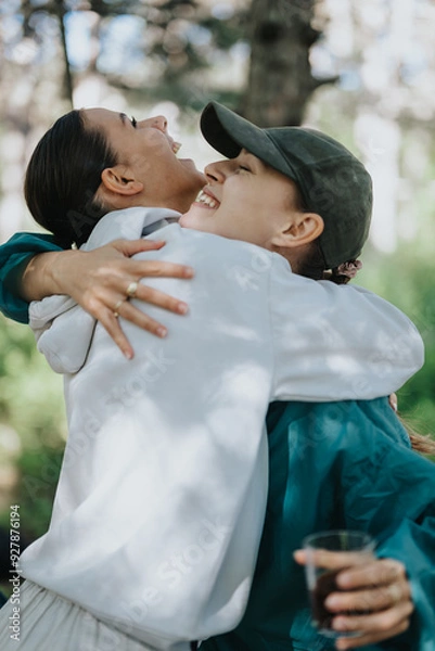 Fototapeta Two friends embracing happily in a forest, showcasing emotions of joy, affection, and companionship in a natural outdoor setting.