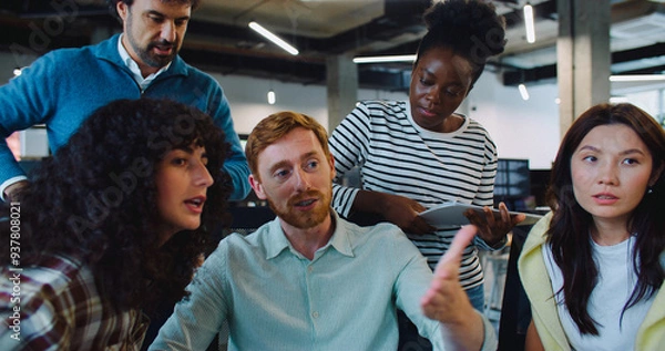 Fototapeta Tired Caucasian man sitting on chair while talking with his office coworkers. Trying to explain crucial decision. People not agreeing. Cutting salary or adding working days. People not happy.