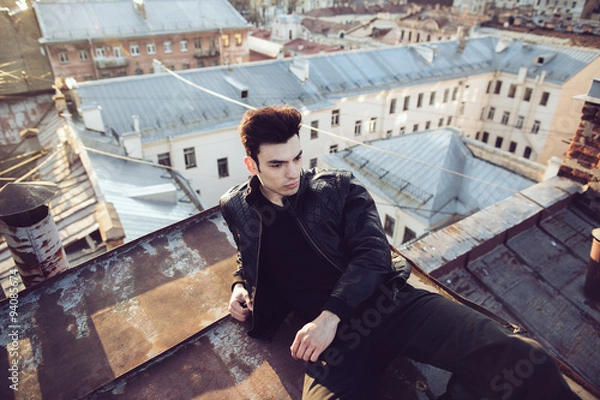 Fototapeta Man in a leather jacket on a rooftop in the center of the city