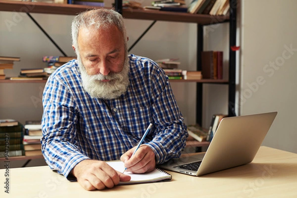 Fototapeta senior man writing in notepad at his working place