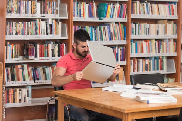 Fototapeta Confused Male Student Reading Many Books For Exam