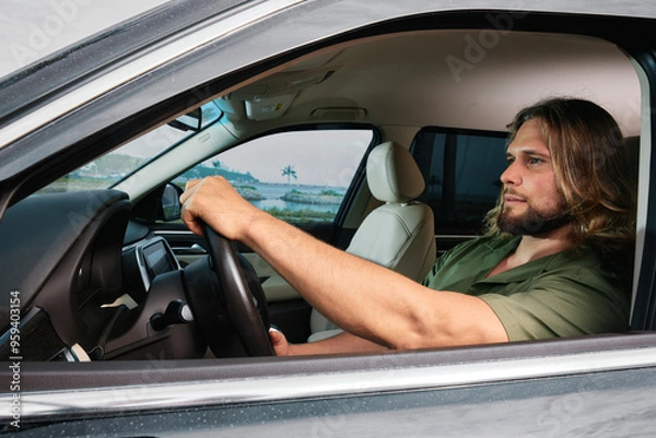 Fototapeta Man driving a car with a focused expression, surrounded by nature in a coastal setting