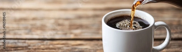 Fototapeta hot coffee being poured into a white mug on a rustic wooden table, evoking warmth and comfort.