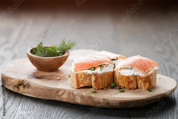 Fototapeta baguette slices with soft cheese and salmon on wood table