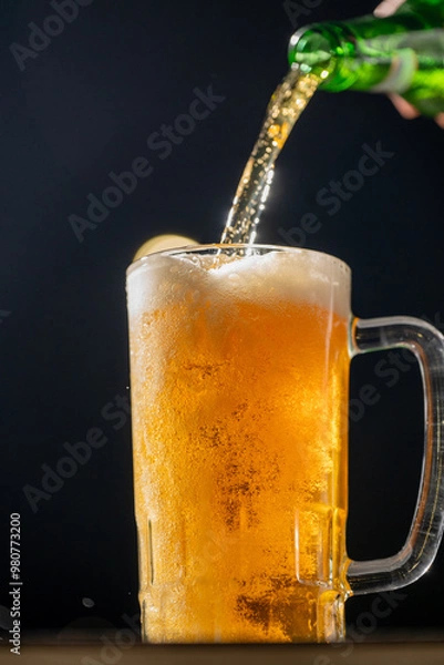 Fototapeta A bright and refreshing beer is being poured into a cold glass mug. The golden liquid, illuminated by a dark background, perfectly captures the celebratory essence of Oktoberfest.