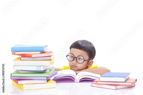 Fototapeta Cute little boy is reading a book with a stack of books.