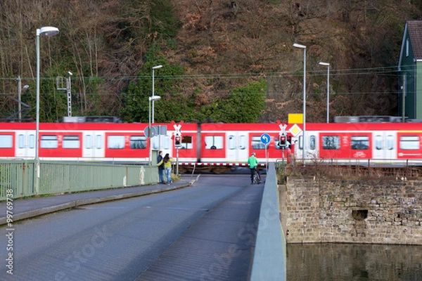 Fototapeta Menschen warten an beschranktem Eisenbahnübergang mit vorbei fahrendem Zug in Bochum Dahlhausen