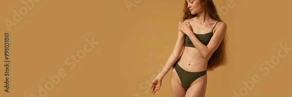 Fototapeta Cropped image of young woman posing in cotton top, showing her healthy and slim body against sandy color studio background. Concept of natural female beauty, body and skin care, health. Banner