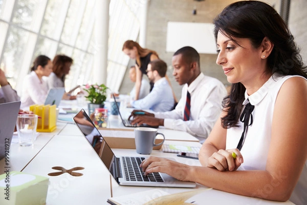 Fototapeta Businesswoman Working On Laptop In Busy Office